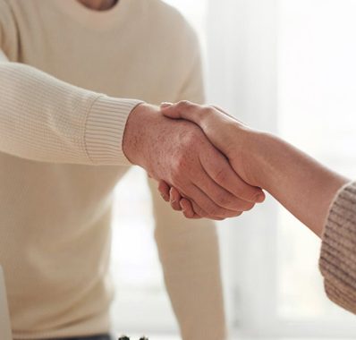 man in white cardigan shaking hands with woman out of frame
