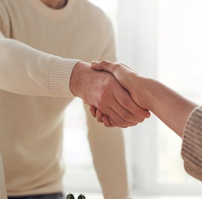 man in white cardigan shaking hands with woman out of frame